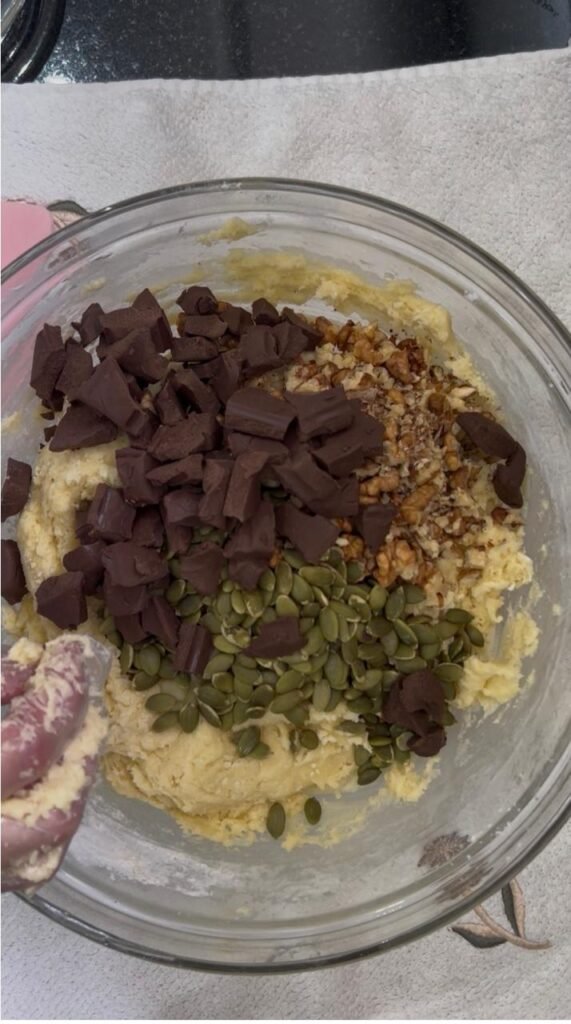 Chopped chocolate chunks added to walnut and pumpkin seed cookie dough