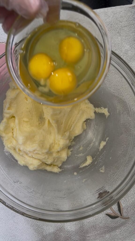 Three eggs being added to creamed butter and sugar for cookie dough