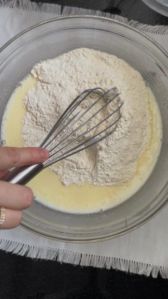 Flour whisked into buttermilk crepe batter in a glass bowl