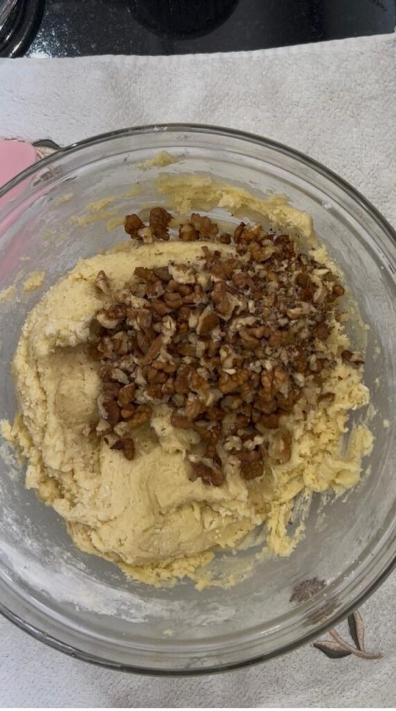 Crushed toasted walnuts added to cookie dough in a glass bowl