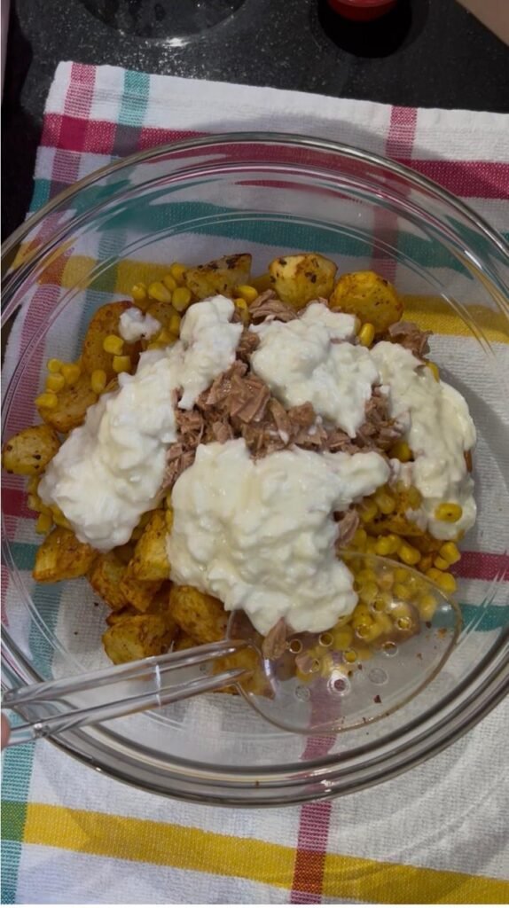 Yogurt dressing poured over potato salad with tuna and corn