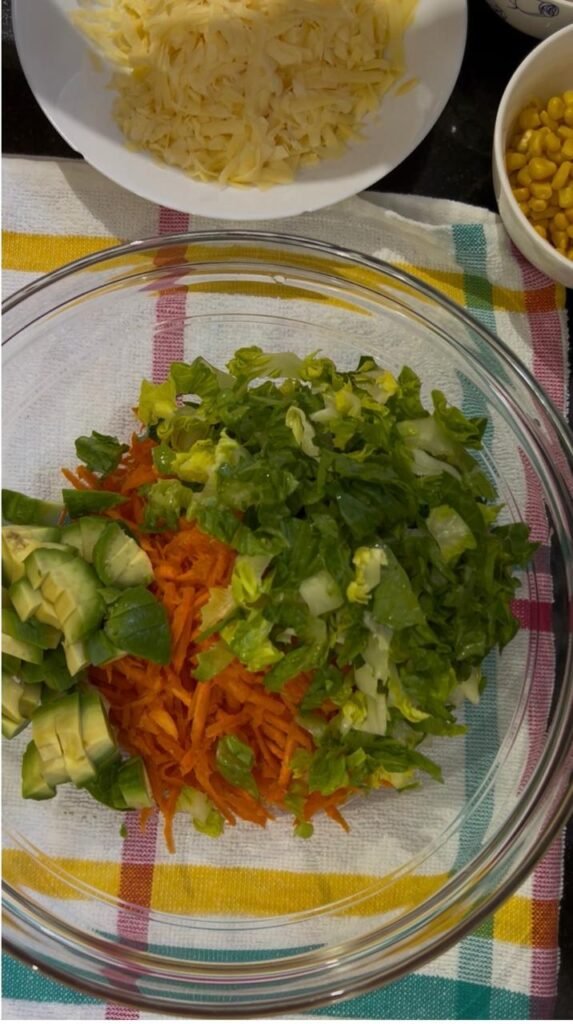 Grated carrot, chopped lettuce and diced avocado in a glass mixing bowl