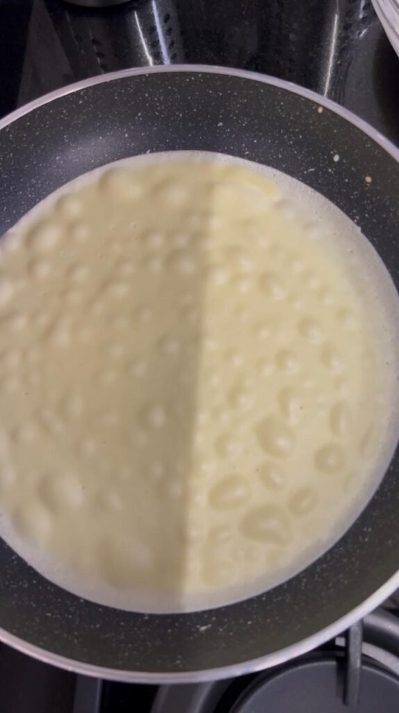 Thin crepe cooking in a non-stick pan with golden freckles