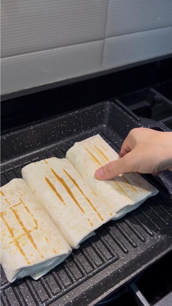 Three tuna wraps grilling on a hot grill pan with golden stripes