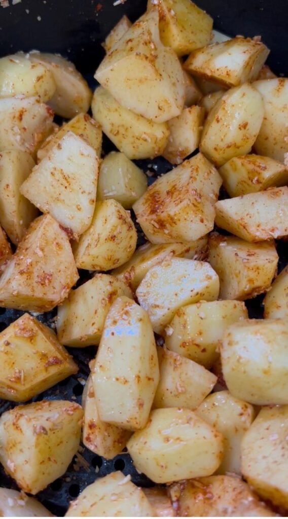 Seasoned potato cubes spread in an air fryer basket ready to cook