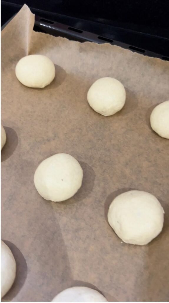 Eighteen shaped banana dough balls on a parchment lined baking sheet