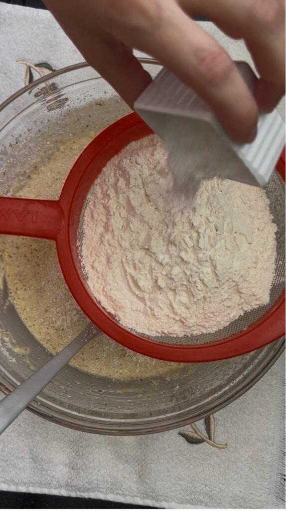 Sifting flour and baking powder into the almond batter