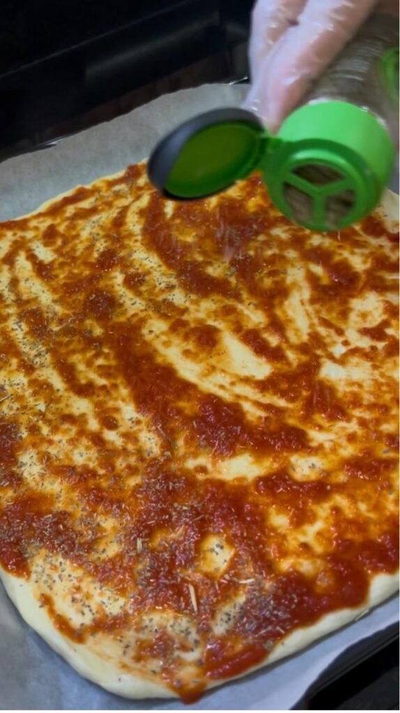 Tomato sauce and dried oregano spread over the pizza base