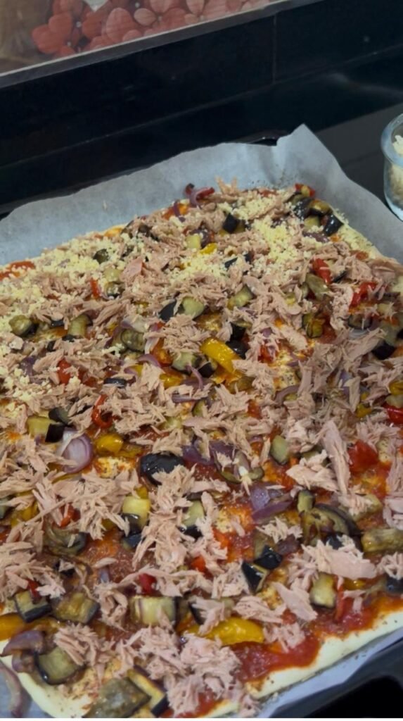 Drained tuna scattered over the vegetables on the pizza