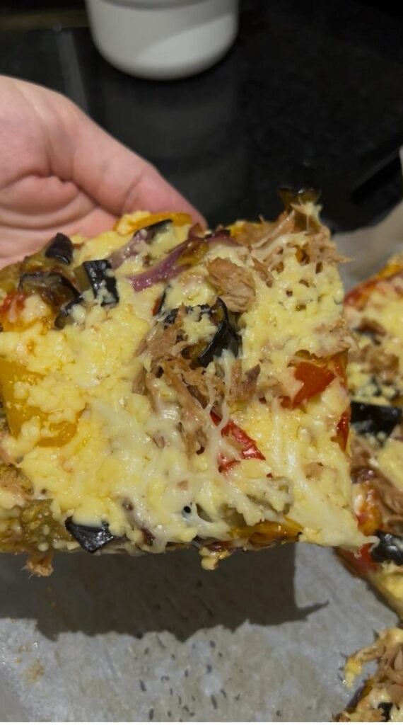 A hand holding a slice of high protein veggie pizza