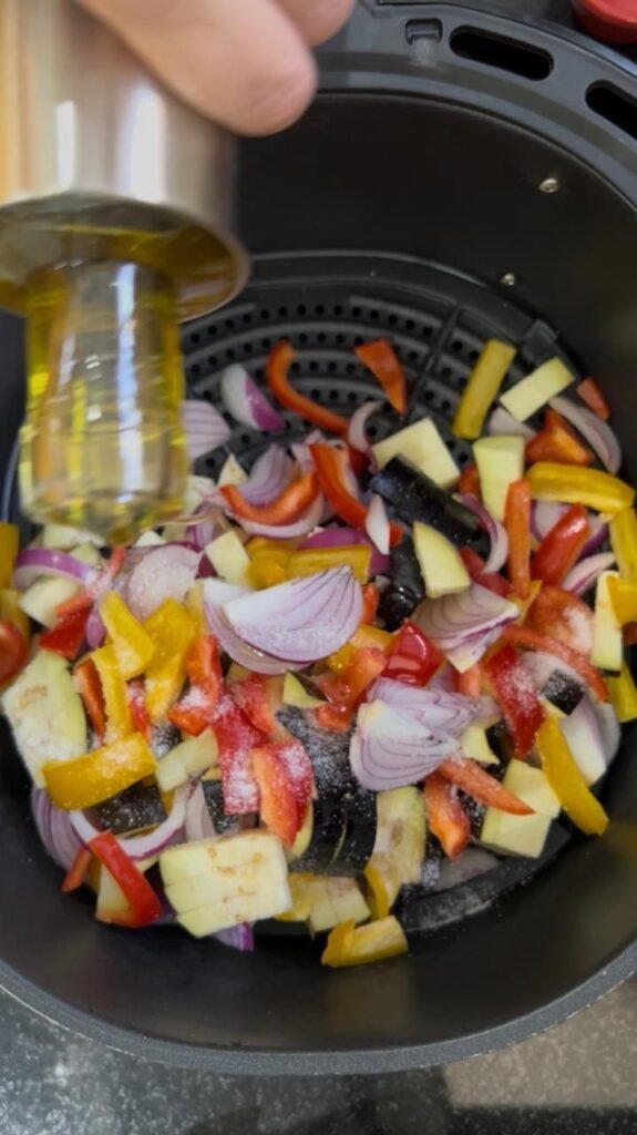 Raw vegetables tossed with olive oil in the air fryer basket