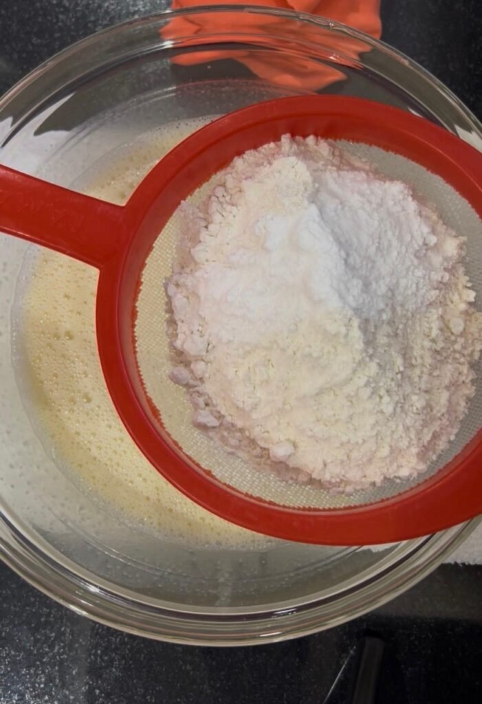 Sifting flour and baking powder into banana cake batter to prevent lumps