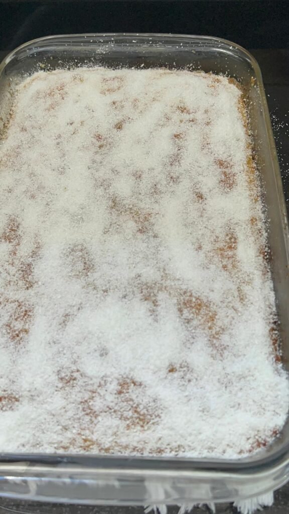 Shredded coconut scattered over orange basbousa cake
