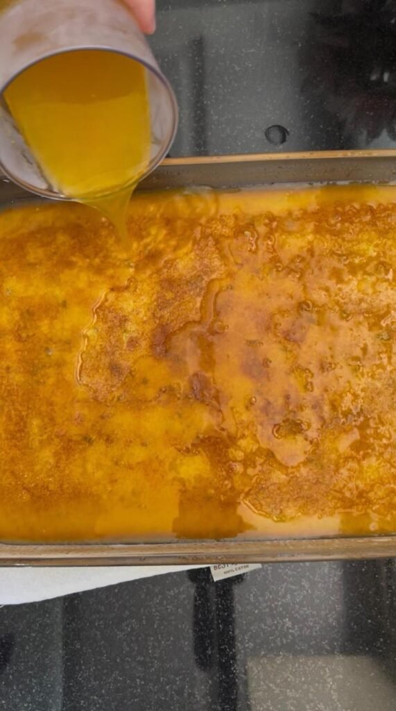 Cold orange syrup being poured over hot basbousa cake