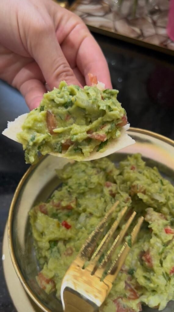 Creamy homemade guacamole on a tortilla chip, showing texture and fresh parsley garnish