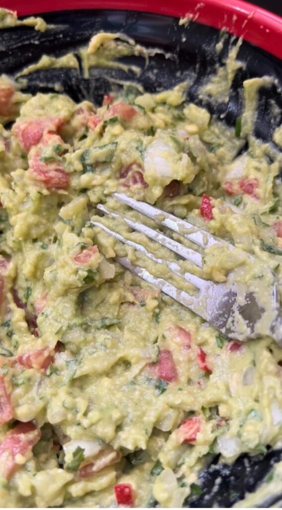 Folding fresh vegetables and parsley into mashed avocado for homemade guacamole