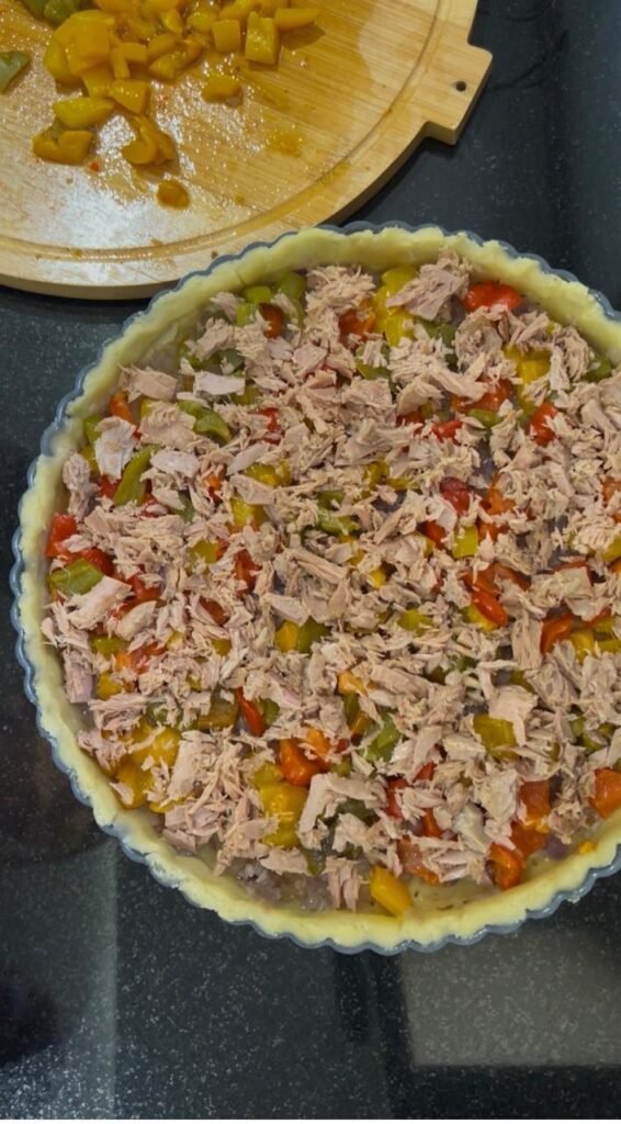 Flaked tuna scattered over roasted peppers in a tart pan