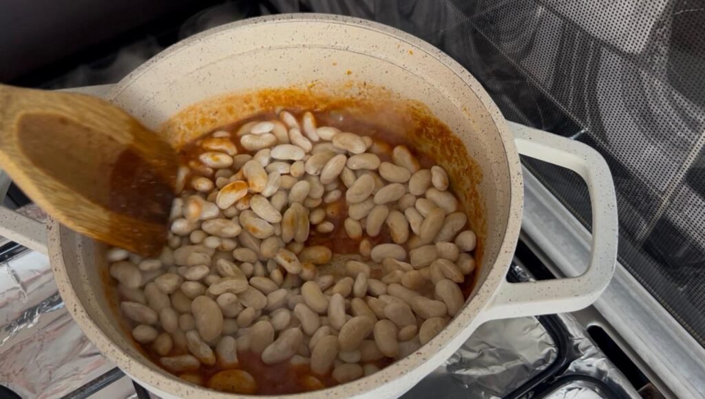White beans mid-cook in aromatic broth showing tender texture and even distribution during easy white bean stew simmer, with wooden spoon visible