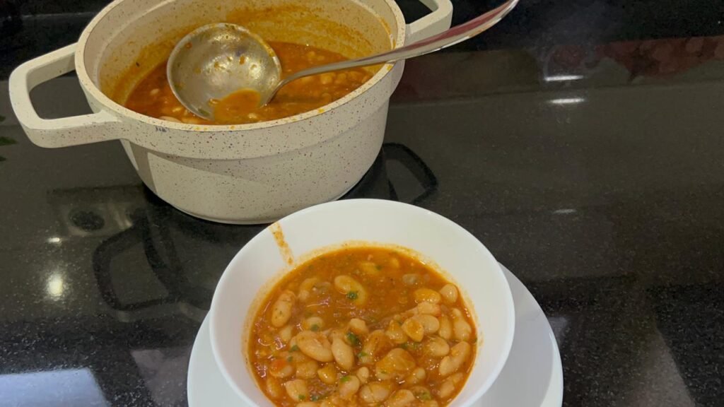 Hearty white bean stew finished with fresh parsley shown in serving pot and white bowl