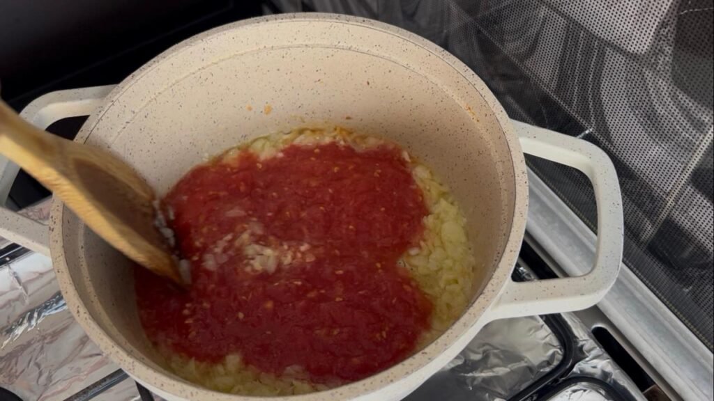 Grated tomatoes with coriander, ginger, paprika, and salt simmering in olive oil in pot, building the flavor base for one-pot white bean stew