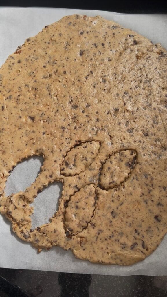 Cookie shapes cut with cutters from chocolate walnut sablé dough on parchment paper