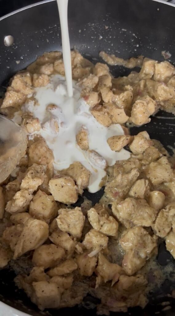 Heavy cooking cream being poured into chicken and onion pan for easy creamy chicken penne silky sauce