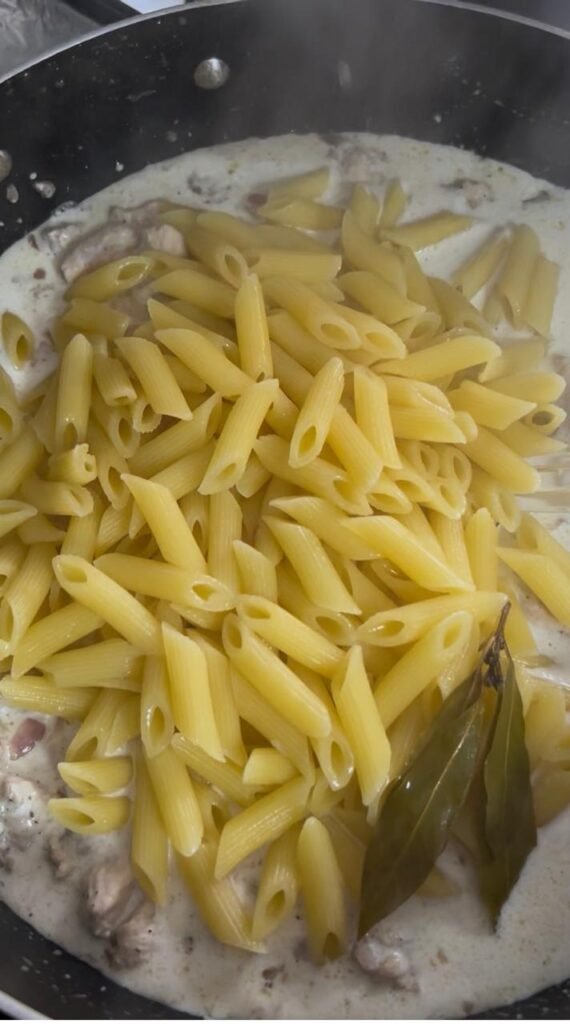 Boiled penne pasta being tossed into creamy chicken sauce for easy creamy chicken penne