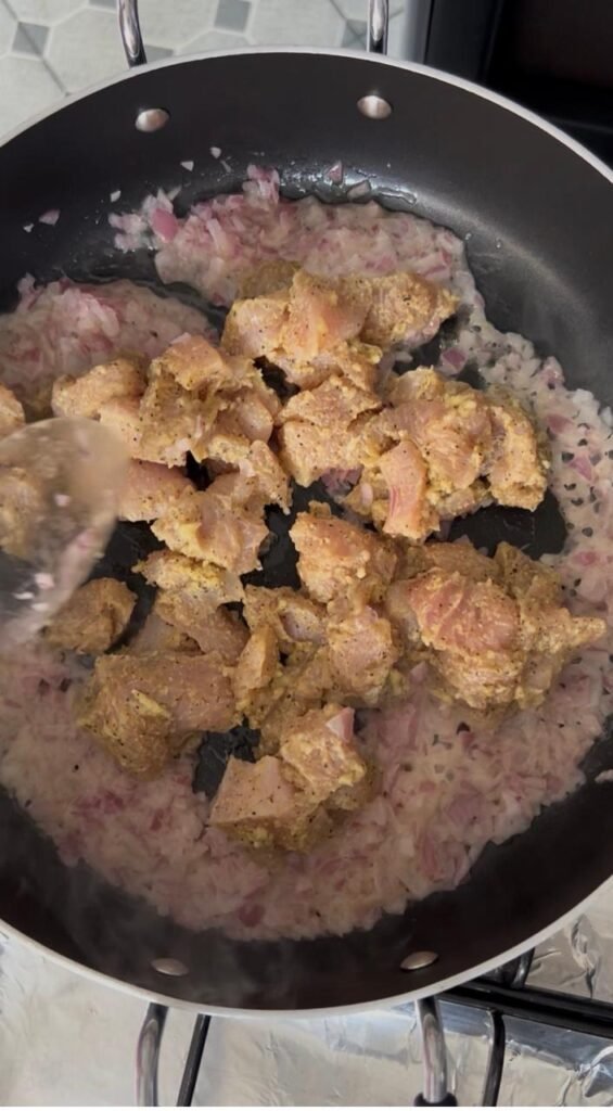 Marinated chicken pieces browning in pan with sautéed onions for easy creamy chicken penne