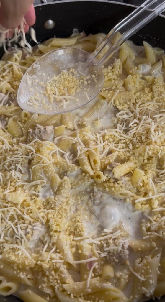 Shredded cheese melting into creamy chicken penne sauce, creating luxurious coating
