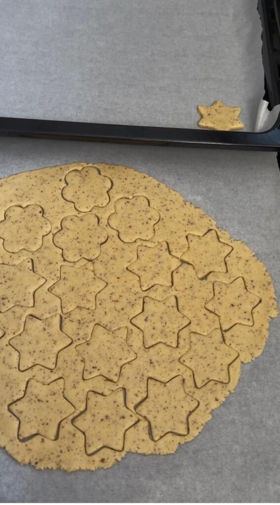 Golden almond sablé cookie dough cut into star and flower shapes with cookie cutters on parchment paper