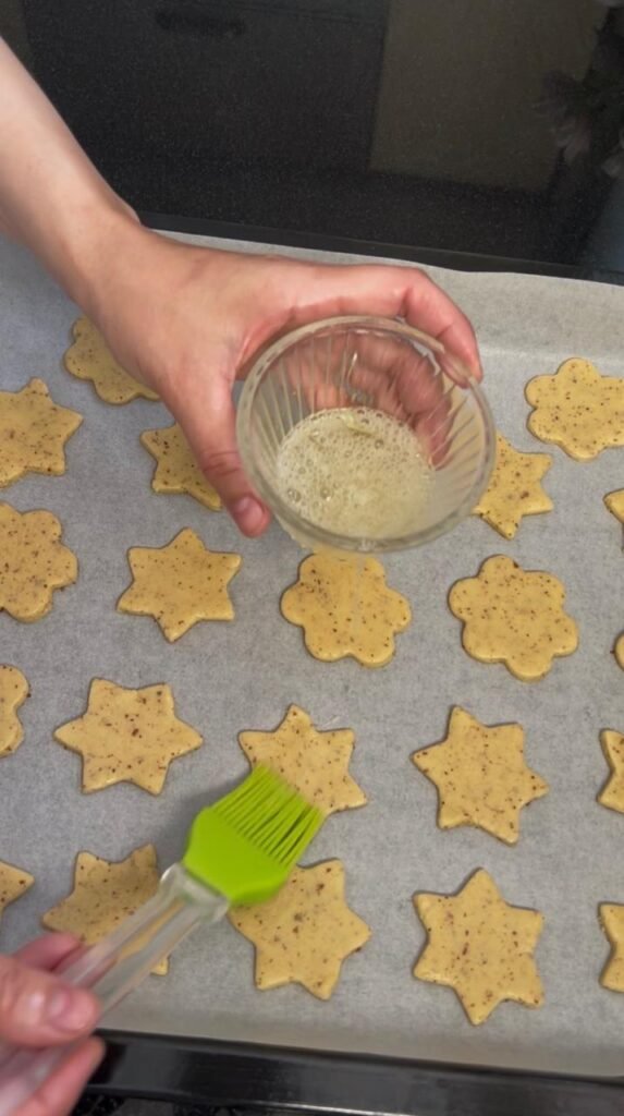 Beaten egg white being brushed onto golden almond sablé cookie dough shapes for golden glaze finish