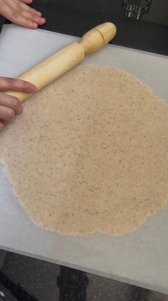 Dough being rolled out between parchment paper sheets for golden almond sablé cookies, showing even ¼-inch thickness