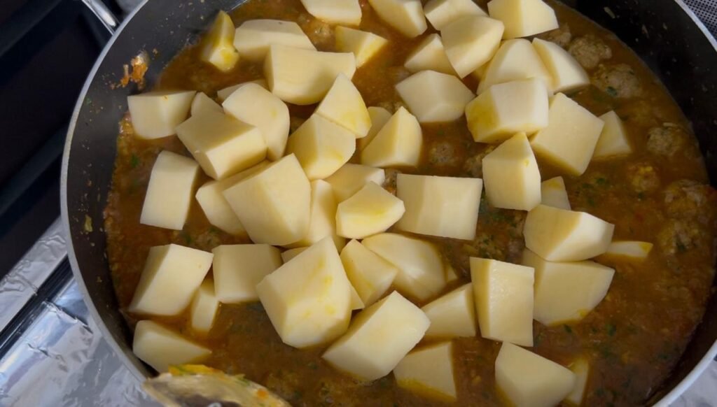 Potato chunks added to easy meatball and potato stew ready to simmer