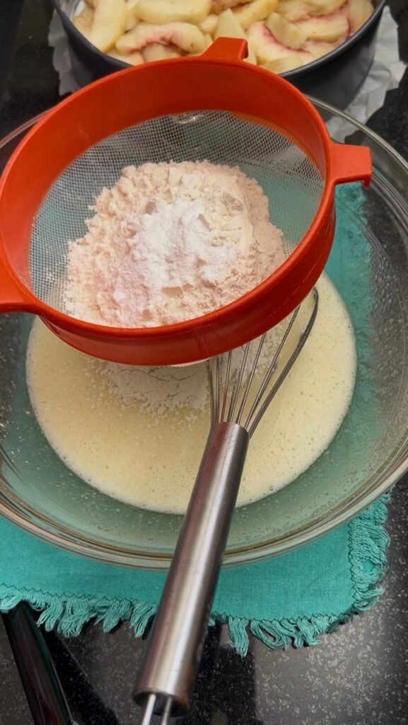 Flour and baking powder sifted over wet ingredients for easy peach cake
