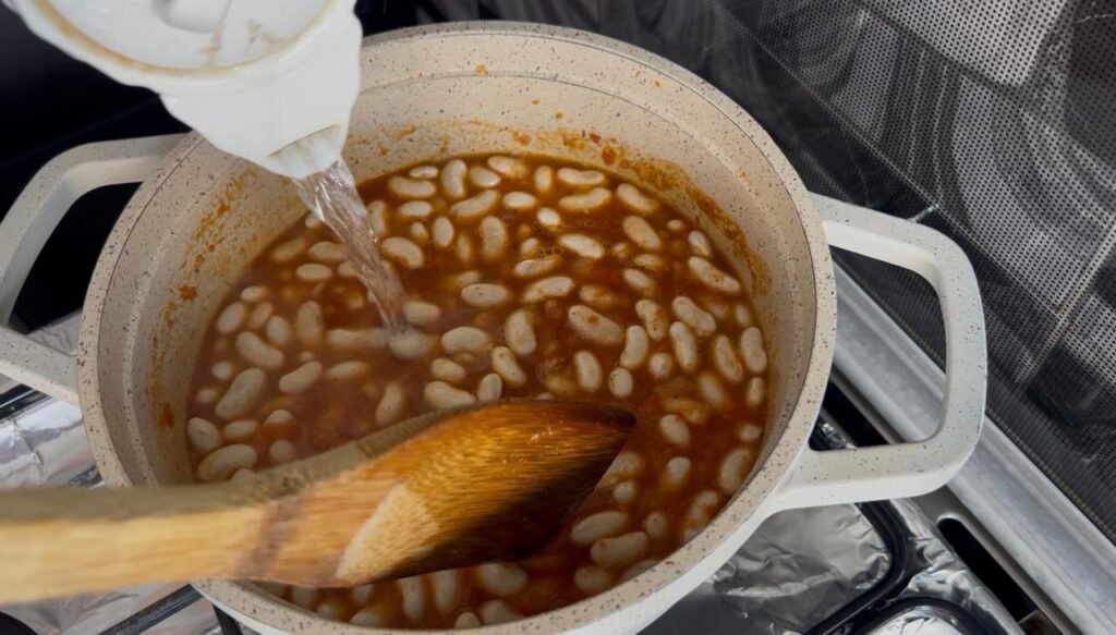 White beans simmering in russet-colored broth with wooden spoon stirring, showing tender texture during easy white bean stew one-hour cook time